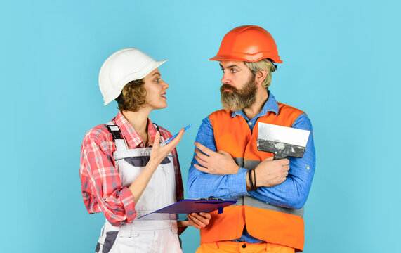 two parters. couple looking at a blueprint. woman and man wear safety hardhat. family standing inside house under construction. renovation and people concept. Builder Couple Look At Home Plans