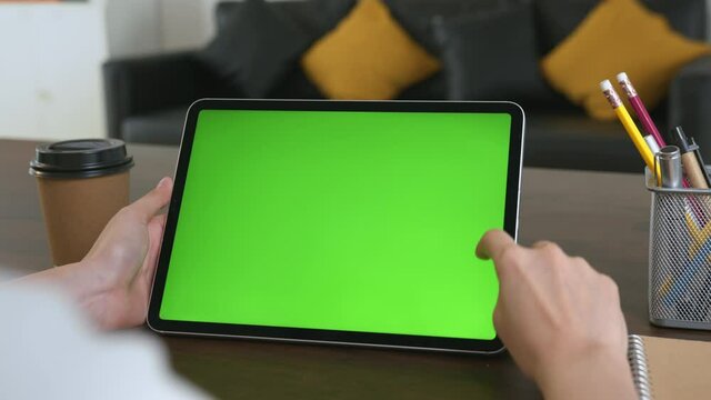 Woman holding digital tablet with green screen and touch device browsing Internet on office desk.