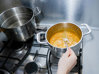 Selective focus on a stainless steel pan on a gas stove. The process of making the sauce. Hand stirs the sauce with a fork. Home kitchen.