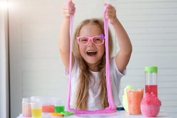 A little girl with glasses is played with a homemade pink slime. Kids hands playing slime toy.