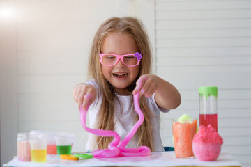 A little girl with glasses is played with a homemade pink slime. Kids hands playing slime toy.