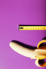 Yellow banana penis concept measured by measuring tape on pink background. Comparison of the size...