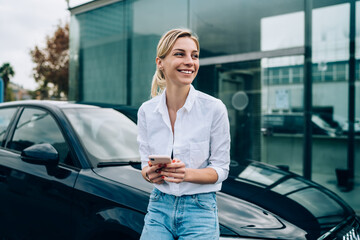 Blonde lady driver texting on smartphone near vehicle
