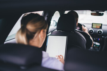Faceless woman with tablet sitting in back car seat behind driver