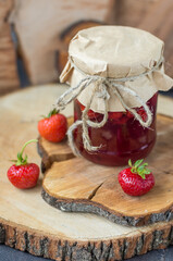 Strawberry jam in a jar on a background of a wooden tray with strawberries in a rustic style vertical arrangement