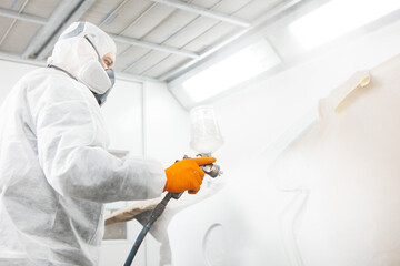 Worker paints auto elements with spray gun. White car in a paint chamber during repair work.