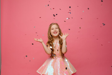 happy Little girl catches confetti on pink background, holiday concept