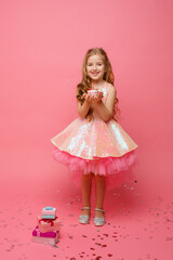 a little girl blows out a candle on a birthday cake in a Studio on a pink background. A child is celebrating a birthday on a pink background