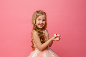Obraz na płótnie Canvas a little girl blows out a candle on a birthday cake in a Studio on a pink background. A child is celebrating a birthday on a pink background