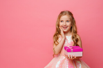 a little girl holding a gift in her hands smiles on a pink background.