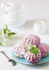 Homemade berry marshmallows on a blue plate with a apple tree flowers  and three tea cups on a white table. Selective focus. Front view