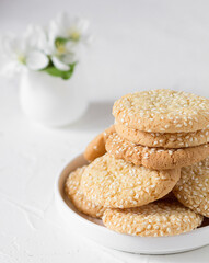 Freshly baked round sesame cookies with a apple tree flowers on a white table. Selective focus. Front view