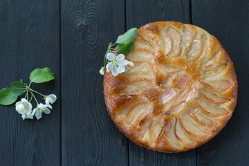 Freshly baked apple pie with apple tree flowers on a black table. Top view