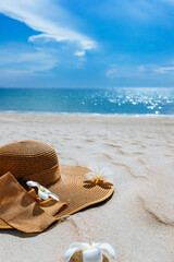 Straw hat with seashells and frangipani flowers on white sea sand. With beautiful seascape, the blue sea in the background