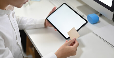 A young smart man is shopping online with a computer tablet at the white working desk.