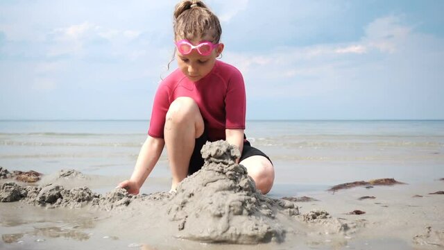 Pretty happy teen child girl in neoprene swimsuit building sand castle on beach at Baltic sea in Germany