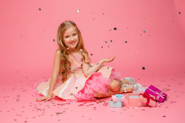 Obraz na płótnie Canvas a little blonde girl with long hair is sitting with gifts on a pink background. Birthday. A child is celebrating a birthday on a pink background