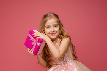 a little girl holds a gift in her hands on a pink background