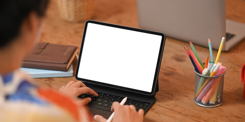 Cropped image hands are using a white blank screen computer tablet with a keyboard case.