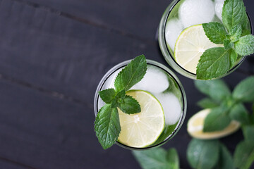 Two glasses of homemade citrus lemonade mojito with slices of lime, mint and ice on a dark wooden background.Top view.