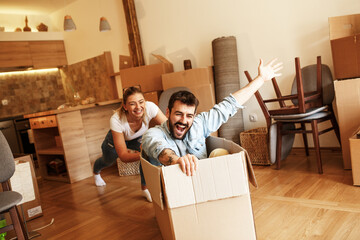 Young married couple moving into a new home.Man sitting in cardboard box while woman pushes him all over the room.Real estate funny concept
