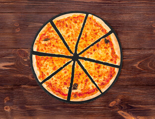 Sliced margherita pizza with mozzarella, bocconcini and basil leaves on slate round platter which is on wooden background, top view