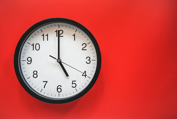 Classic black and white analog clock on red background at Five o'clock with copy space