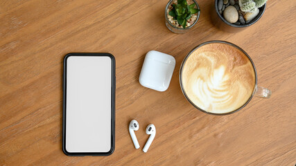 Top view a cup of coffee, smartphone, earphone, cactus and blank screen smartphone on wooden table in home office.