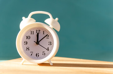 White alarm clock stands on a wooden table on a blue background in the sunlight, copy space