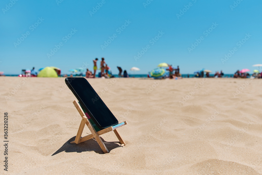 Wall mural smartphone in a deck chair on the beach