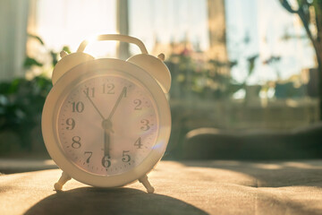 white alarm clock stands on the sofa in the sunlight. Beautiful background with alarm clock