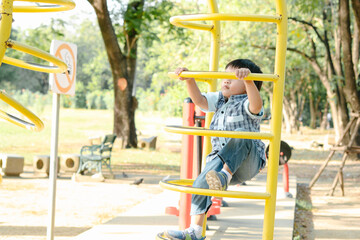 Asian little boy trying to climbs up the curve frame on the playground