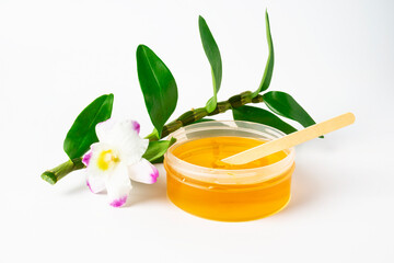 Obraz na płótnie Canvas Yellow sticky sugaring wax paste for hair removing with wooden spatula stick and violet and green orchid flower. Light background with copyspace for text