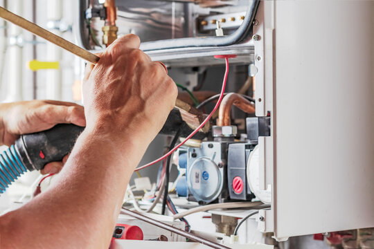 The master sets up a gas boiler, which weighs on the wall. The front dashboard is open. Using a brush and an industrial vacuum cleaner, cleaning from dirt and dirt.