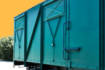 Abstract picture of a green windowless wagon in front of an artificial sky with orange color, concept