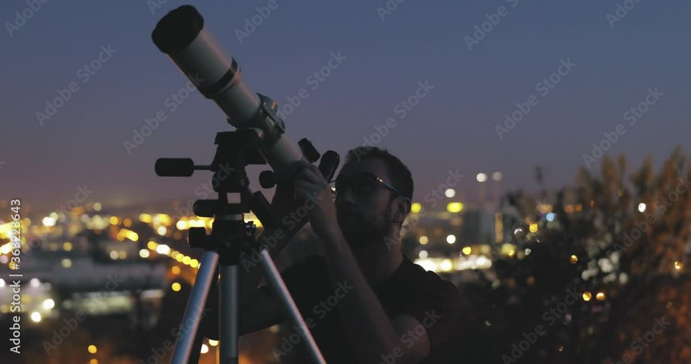 Wall mural astronomer with a telescope watching at the stars and moon with blurred city lights in the backgroun