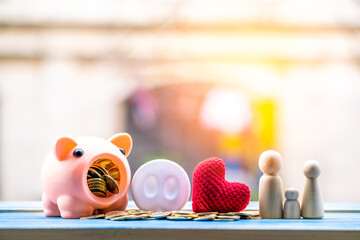 Stacking coins and piggy bank and wooden family and red heart put on the wood on the morning sunlight in public park, Saving money and loan for business investment concept.