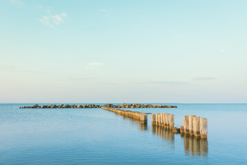 Fototapeta premium Calm morning sea surface with old stone pier and rocks. Morning seascape.