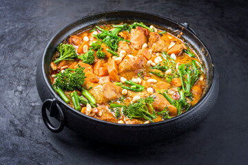 Modern style African crocodile cheeks curry with sweet potato, broccoli and peanuts as close-up in a modern design cast iron pot