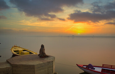 A person is meditating on the bank of river ganga on the ghats of varanasi while sun is rising 