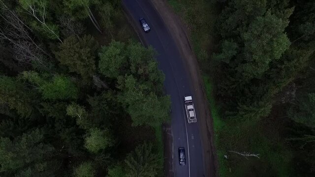 Aerial view of a large tow truck carries a broken car along a forest road.