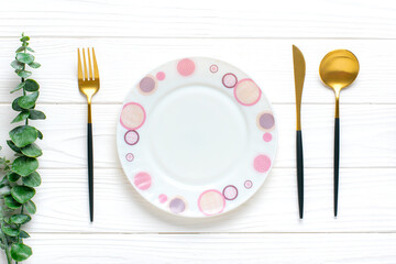 empty white round plate, fork, knife, spoon, sprig of eucalyptus on wooden table Top view Flat lay Dishes for breakfast, lunch or dinner Mock up
