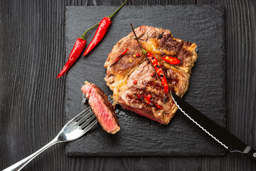 Sliced grilled meat barbecue steak Striploin with knife and fork carving set on black stone slate