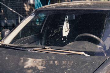 A medical mask is hanging on the rear view mirror of a parked car and symbolizes the end of the pandemic.