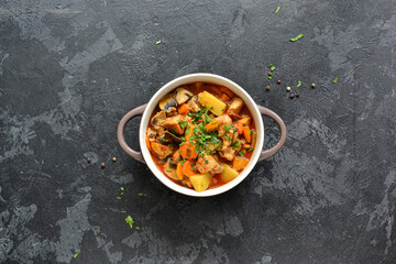 Stew with chicken, potatoes, onions, mushrooms, tomatoes and carrots, and parsley. Vegetable stew. Dark background. Top view.
