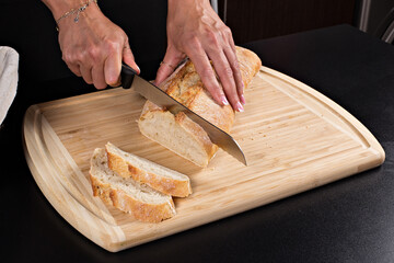 Beautiful woman cuts fresh bread on a wooden board, on a black table in a black dress. Different views