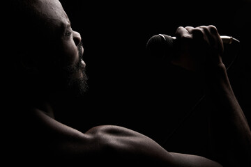portrait of a dark-skinned muscular handsome guy with a beard on a black background who emotionally...