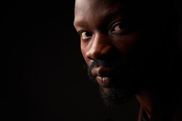 portrait photo of a dark-skinned handsome guy with a beard looking at the camera with serious face on a black background