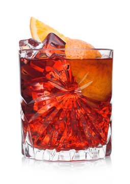 Negroni Cocktail in crystal glass with ice cubes and orange slices on white background with reflection.