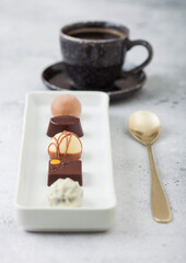 Luxury Chocolate candies in white porcelain plate with cup of black coffee and desset spoon on light table background.